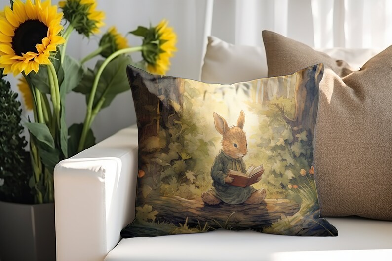May include: A throw pillow with a watercolor illustration of a brown rabbit sitting on a log in a forest, reading a book. The rabbit is wearing a blue dress and has a red book in its paws. The background is a green forest with a sunbeam shining through the trees.