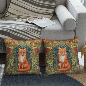 May include: Two decorative throw pillows with a fox illustration surrounded by flowers and greenery. The pillows are on a gray couch with a striped throw blanket.