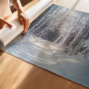 Puede incluir: Una impresi&oacute;n de paisaje invernal con un bosque cubierto de nieve y altos abedules blancos. La impresi&oacute;n se est&aacute; desenrollando sobre una superficie de madera, revelando un camino a trav&eacute;s del bosque nevado. La paleta de colores es principalmente blanca, azul y gris.