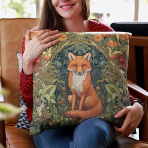 May include: A throw pillow with a green, orange, and brown fox illustration surrounded by floral designs. The fox is sitting in a forest setting with leaves and flowers.