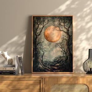 Puede incluir: Una impresi&oacute;n enmarcada de una pintura que representa una gran luna naranja elev&aacute;ndose sobre un paisaje boscoso oscuro. La luna est&aacute; parcialmente oscurecida por los &aacute;rboles, creando una sensaci&oacute;n de misterio y asombro.