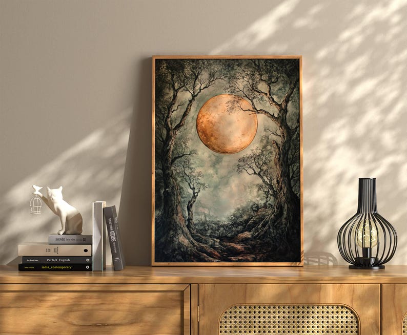 Puede incluir: Una impresi&oacute;n enmarcada de una pintura que representa una gran luna naranja elev&aacute;ndose sobre un paisaje boscoso oscuro. La luna est&aacute; parcialmente oscurecida por los &aacute;rboles, creando una sensaci&oacute;n de misterio y asombro.