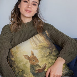 May include: A green knitted sweater with a throw pillow featuring a watercolor illustration of a rabbit reading a book in a forest setting.