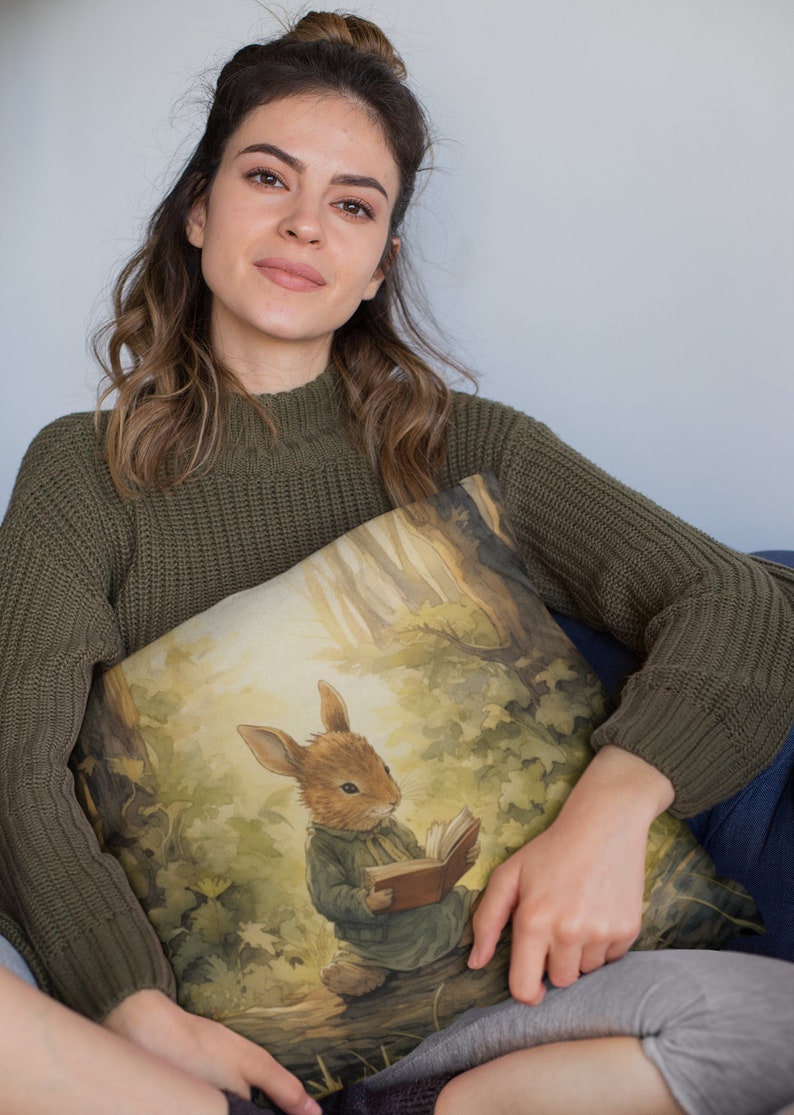 May include: A green knitted sweater with a throw pillow featuring a watercolor illustration of a rabbit reading a book in a forest setting.