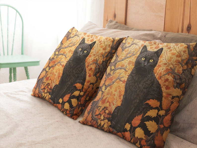 Pu&ograve; includere: Due cuscini decorativi con un gatto nero seduto in un bosco di foglie autunnali. I cuscini sono su un letto con un copripiumino bianco.