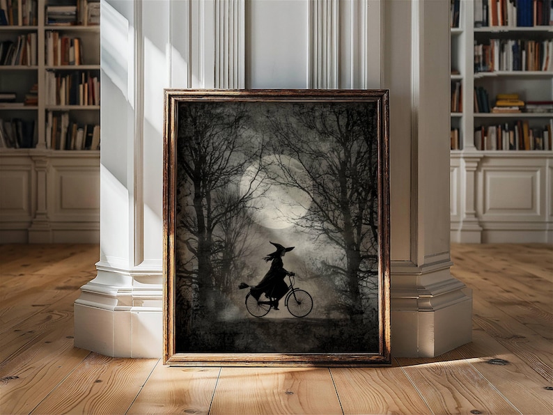K&ouml;nnte beinhalten: Gerahmtes Kunstwerk mit einer Silhouette einer Hexe, die durch einen mondbeschienenen Wald Fahrrad f&auml;hrt. Das Kunstwerk hat eine dunkle, stimmungsvolle &Auml;sthetik mit einem Vollmond im Hintergrund und kahlen B&auml;umen. Der Rahmen ist warmbraun.