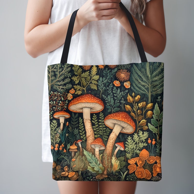 This gorgeous William Morris inspired tote bag design features detailed mushrooms growing from the forest floor.  The mushrooms have orange caps with yellow speckles.  The mushrooms are surrounded by lush vegetation.