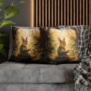 May include: Two decorative throw pillows with a woodland scene featuring a brown rabbit reading a book. The pillows are on a gray couch with a black and white throw blanket.