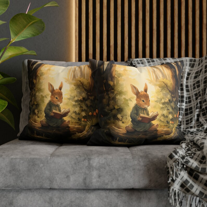 May include: Two decorative throw pillows with a woodland scene featuring a brown rabbit reading a book. The pillows are on a gray couch with a black and white throw blanket.