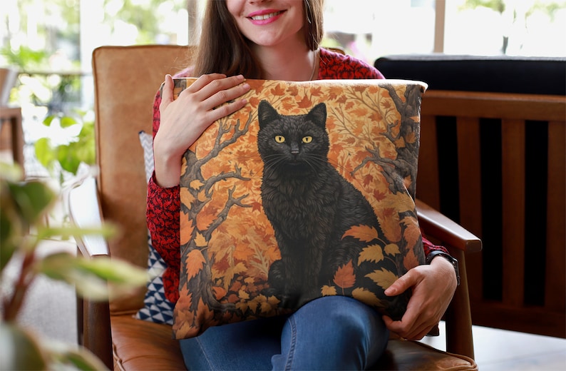 Pu&ograve; includere: Un gatto nero con gli occhi gialli seduto in una foresta di foglie arancioni e marroni. Il gatto &egrave; raffigurato su un cuscino con uno sfondo marrone.