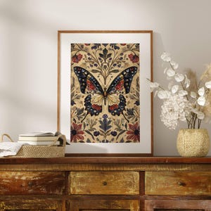 Puede incluir: Una impresi&oacute;n art&iacute;stica enmarcada con una ilustraci&oacute;n detallada de una mariposa. La mariposa tiene alas negras, rojas y amarillas, sobre un fondo floral con acentos burdeos y azul marino. La obra de arte se exhibe en una c&oacute;moda de madera.