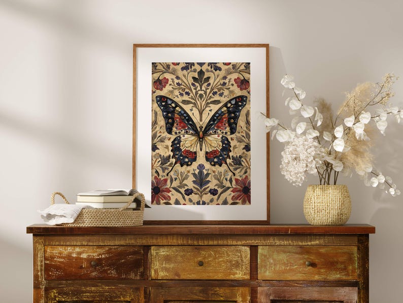 Puede incluir: Una impresi&oacute;n art&iacute;stica enmarcada con una ilustraci&oacute;n detallada de una mariposa. La mariposa tiene alas negras, rojas y amarillas, sobre un fondo floral con acentos burdeos y azul marino. La obra de arte se exhibe en una c&oacute;moda de madera.