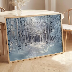 Puede incluir: Impresi&oacute;n enmarcada de un paisaje invernal con un camino cubierto de nieve que serpentea por un bosque de abedules. La obra de arte muestra una escena serena con nieve blanca, sombras azules y un marco dorado, evocando tranquilidad.