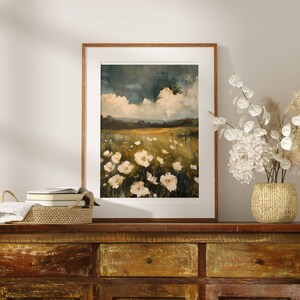 May include: A framed painting of a field of white flowers with a cloudy sky in the background. The painting is hanging on a wall above a wooden dresser.