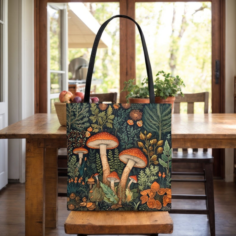 Puede incluir: Una bolsa de lona negra con una ilustraci&oacute;n colorida de setas y follaje. Las setas son rojas y naranjas con manchas blancas. El follaje es verde y marr&oacute;n.