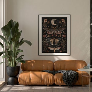 May include: A brown leather sofa with a black throw blanket in front of a white wall with a framed print of moths and flowers on a black background.