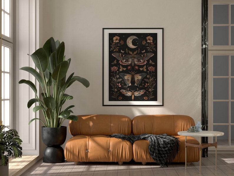 May include: A brown leather sofa with a black throw blanket in front of a white wall with a framed print of moths and flowers on a black background.