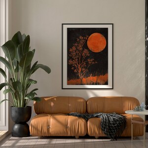 Peut inclure: Un canap&eacute; en cuir marron avec un plaid noir et blanc devant une impression encadr&eacute;e noire d'un arbre et d'une grande lune orange sur un fond sombre.