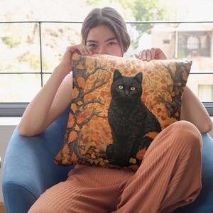 Pu&ograve; includere: Un gatto nero con gli occhi gialli seduto in una foresta di foglie arancioni e marroni. Il gatto &egrave; su un cuscino con un motivo autunnale.