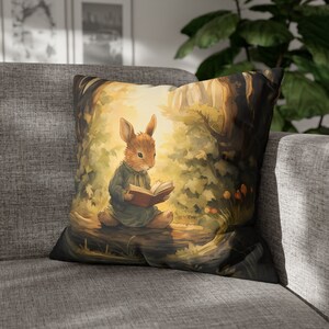 May include: A brown rabbit wearing a blue dress sits on a tree branch in a forest setting. The rabbit is reading a book with a red cover. The background is a soft, watercolor-style illustration of trees and leaves.
