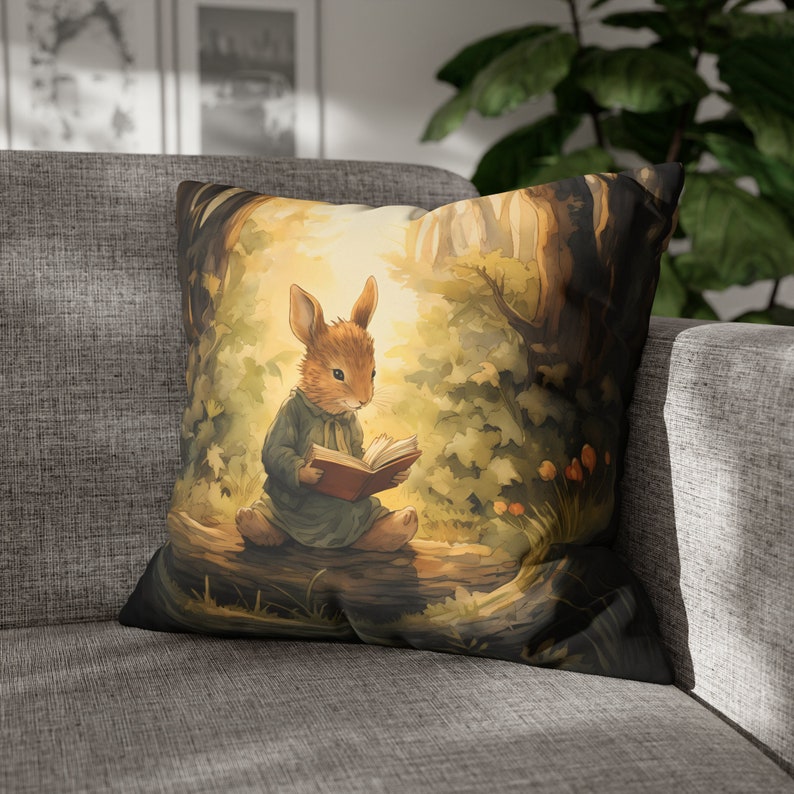 May include: A brown rabbit wearing a blue dress sits on a tree branch in a forest setting. The rabbit is reading a book with a red cover. The background is a soft, watercolor-style illustration of trees and leaves.
