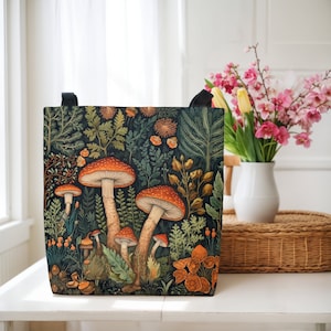 Puede incluir: Una bolsa de lona negra con una ilustraci&oacute;n colorida de setas y follaje. La bolsa tiene una gama de colores verde oscuro, marr&oacute;n y rojo.
