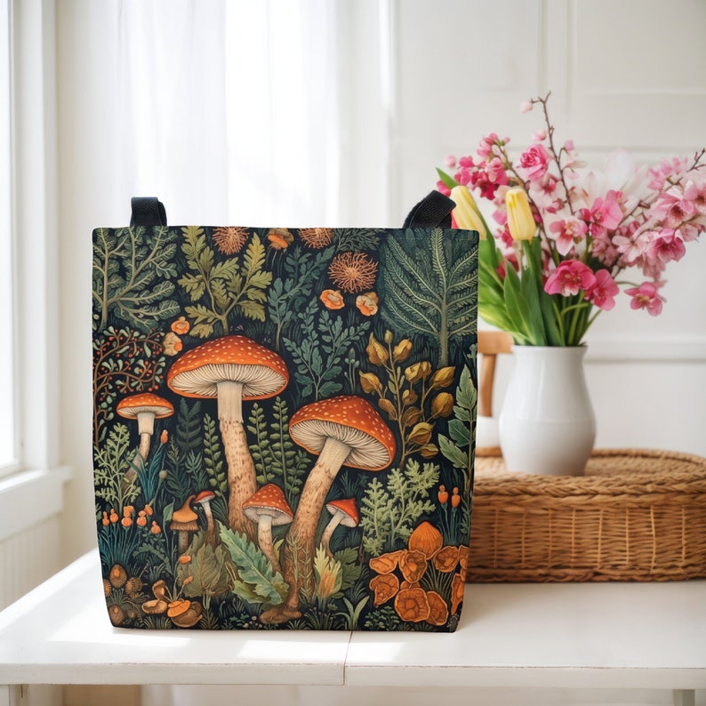 Puede incluir: Una bolsa de lona negra con una ilustraci&oacute;n colorida de setas y follaje. La bolsa tiene una gama de colores verde oscuro, marr&oacute;n y rojo.