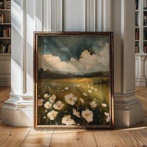 May include: A framed painting of a field of white flowers with a cloudy sky in the background. The painting is in a brown frame and is leaning against a white wall.