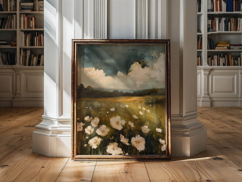 May include: A framed painting of a field of white flowers with a cloudy sky in the background. The painting is in a brown frame and is leaning against a white wall.