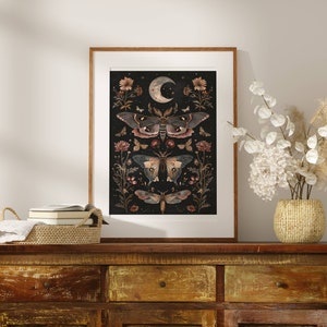 May include: A framed print with a black background featuring a crescent moon and a series of moths and flowers in shades of brown, pink, and white.