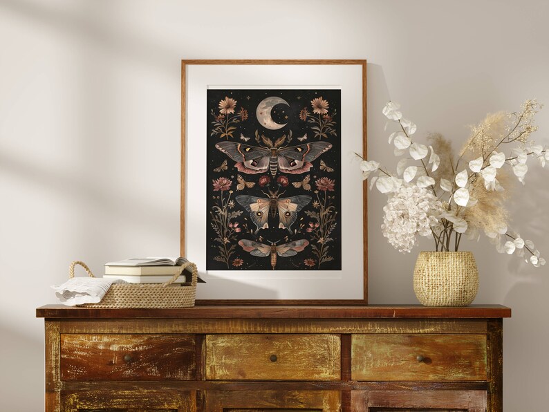 May include: A framed print with a black background featuring a crescent moon and a series of moths and flowers in shades of brown, pink, and white.