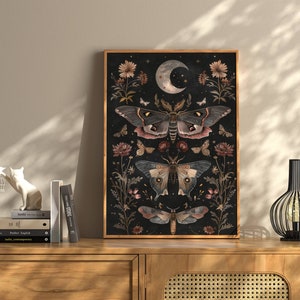 May include: A black and white art print featuring a dark background with three moths and floral details. The moths are in shades of brown, pink, and white. The print has a vintage aesthetic.