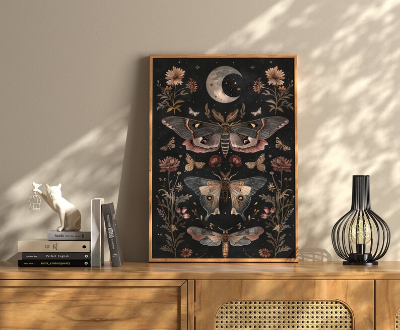 May include: A black and white art print featuring a dark background with three moths and floral details. The moths are in shades of brown, pink, and white. The print has a vintage aesthetic.