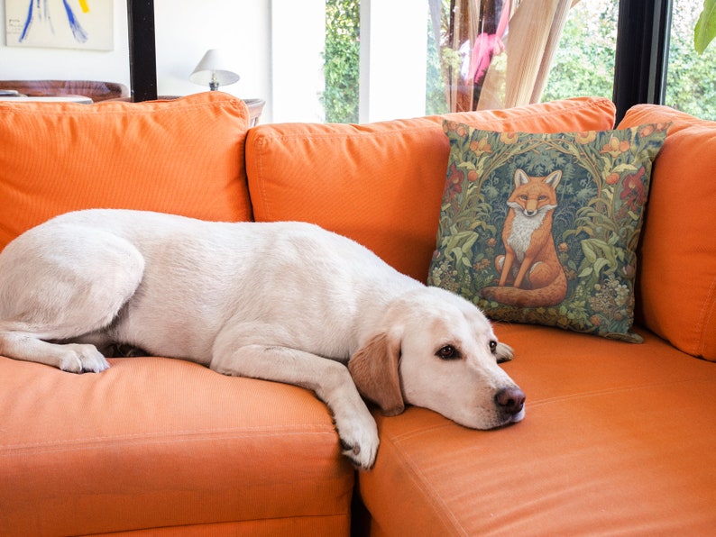 May include: A white dog with brown eyes is lying on an orange couch. A throw pillow with a fox illustration is on the couch behind the dog.