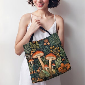 Puede incluir: Una bolsa de tela con asa de lona negra y un estampado colorido de setas y follaje. El estampado presenta setas naranjas y rojas con hojas y flores verdes.