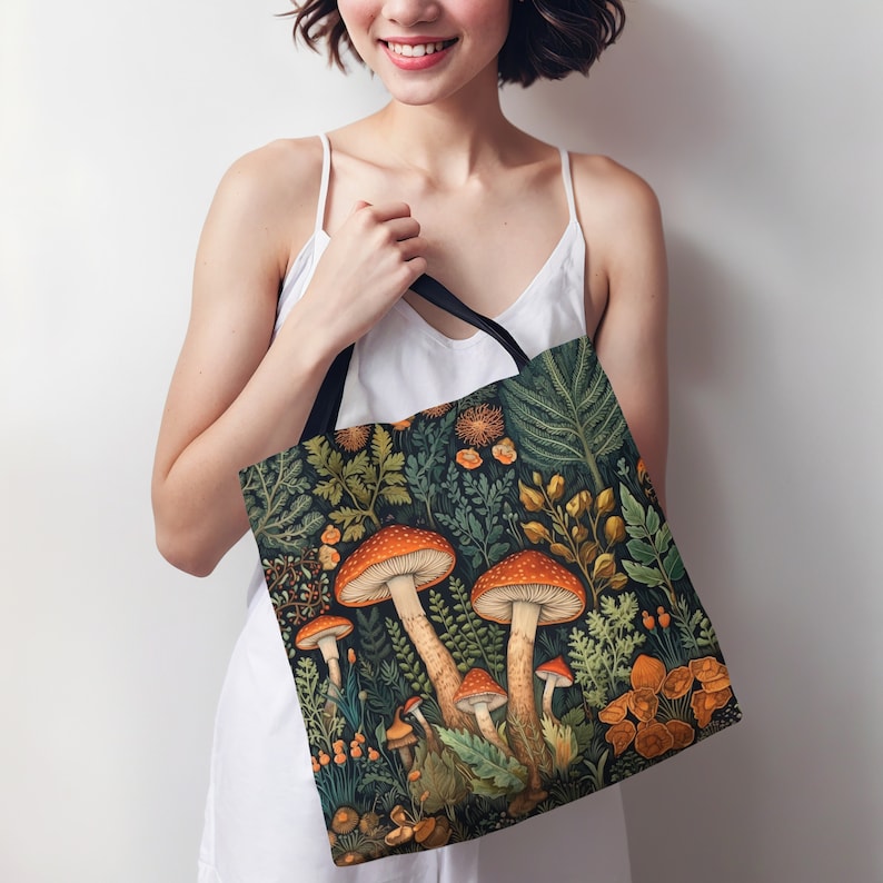 Puede incluir: Una bolsa de tela con asa de lona negra y un estampado colorido de setas y follaje. El estampado presenta setas naranjas y rojas con hojas y flores verdes.