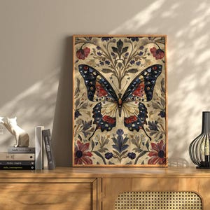 Puede incluir: Una impresi&oacute;n art&iacute;stica enmarcada de una mariposa. La mariposa tiene intrincados patrones en las alas en tonos de azul, rojo y amarillo. El fondo presenta motivos florales y de hojas en tonos apagados. La obra de arte se exhibe en un mueble de madera.