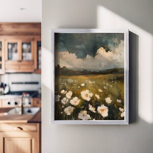 May include: A framed painting of a field of white wildflowers with a cloudy sky in the background. The painting is in a white frame and is hanging on a white wall.