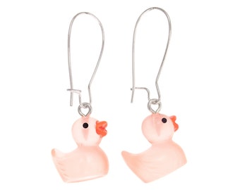 May include: A pair of drop earrings featuring translucent light pink rubber duck charms. Each duck has a small black eye and an orange beak. The charms are suspended from silver-toned metal ear wires with a simple hook design for secure attachment.