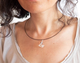 May include: A clear, translucent duck-shaped pendant made of glass or crystal, suspended from a thin, black circular cord necklace. The small, minimalist charm features a smooth, rounded silhouette and is attached to the cord with a silver-toned metal bail.