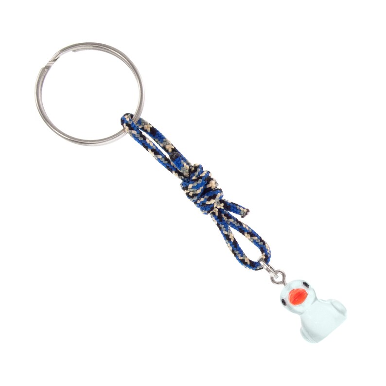 May include: A keyring featuring a silver metal ring attached to a blue, black, and tan braided cord tied in a knot. A small, light blue duck charm with a bright orange beak and black eyes hangs from the end of the cord by a silver jump ring.