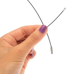 May include: A thin black flexible cable featuring a small metallic screw-on connector at one end and a textured cylindrical metal fastener at the other end, designed for securing items together with a secure threaded locking mechanism.
