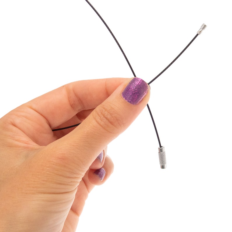 May include: A thin black flexible cable featuring a small metallic screw-on connector at one end and a textured cylindrical metal fastener at the other end, designed for securing items together with a secure threaded locking mechanism.