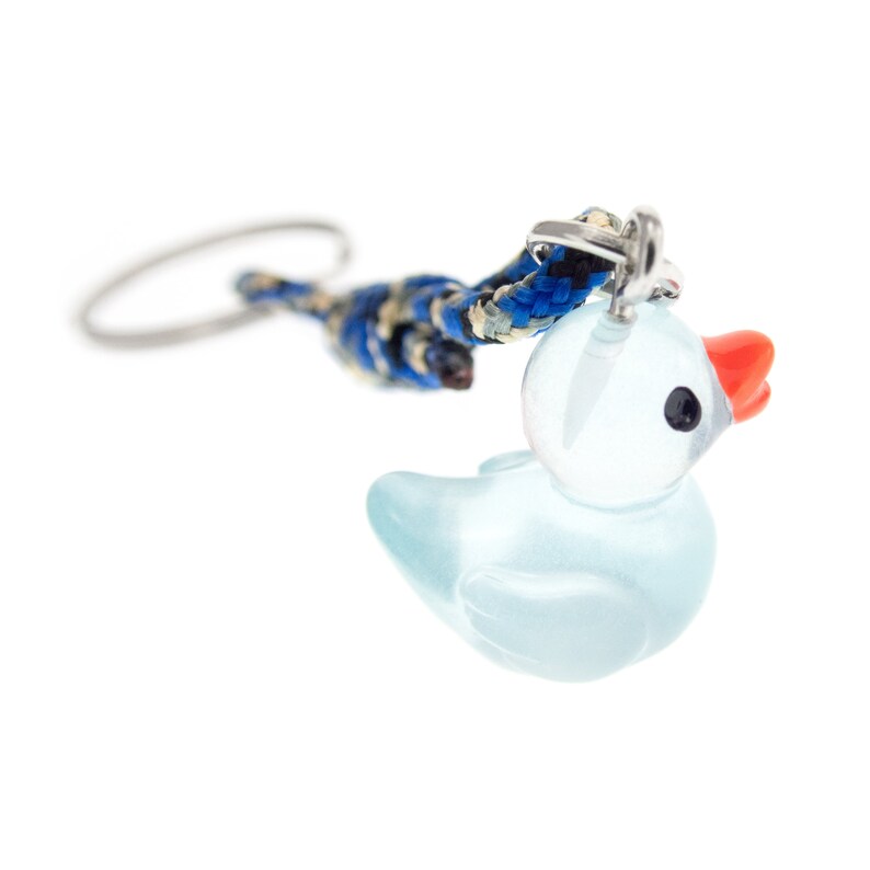 May include: A keyring featuring a translucent light blue glass duck charm with a bright orange beak and black eyes. The charm is attached to a braided cord in shades of blue, black, and tan, which connects to a circular silver metal key ring.