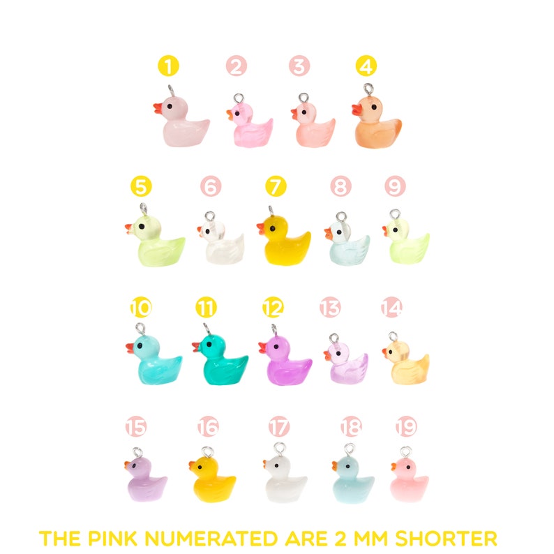 Op de afbeelding: Een verzameling van negentien kleurrijke eendjes, elk met een zilveren lus voor bevestiging. De eendjes zijn in verschillende tinten, waaronder roze, geel, blauw, groen en wit. De tekst onderaan vermeldt dat de roze genummerde eendjes 2 mm korter zijn.