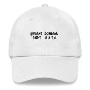 May include: White baseball cap with black embroidered text that reads "Spread Schmeer Not Hate".