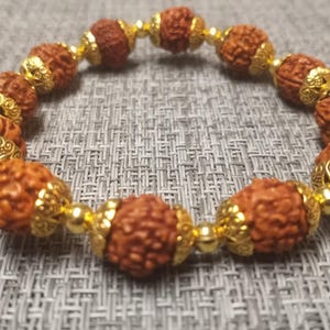 May include: A brown wooden bracelet with gold accents. The bracelet is made of round beads with intricate designs.