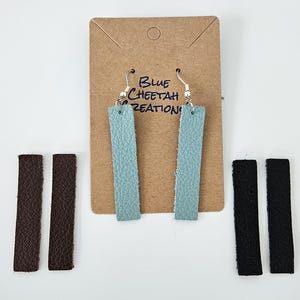Puede incluir: Dos pares de pendientes de cuero en diferentes colores. Los pendientes están en una tarjeta marrón con el texto "Blue Cheetah Creations". El primer par es azul claro, el segundo par es marrón y el tercer par es negro.
