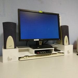 Może przedstawiać: Biały organizer na biurko komputerowe z monitorem, klawiaturą i głośnikami. Organizer ma dwie półki i szufladę. Monitor jest czarny i ma niebieski ekran. Klawiatura jest czarna i ma białe klawisze. Głośniki są czarne i mają srebrną kratkę.