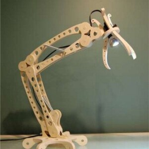 Könnte beinhalten: Eine Schreibtischlampe aus hellem Holz mit einem einzigartigen, beweglichen Design. Die Lampe hat einen geometrischen Rahmen mit einem flexiblen Arm und einer kleinen, runden Leuchte. Der Sockel hat ein sternförmiges Design. Die Lampe ist an eine Steckdose angeschlossen.